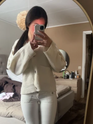 Krämvit  kofta med knappar - Mysig krämvit kofta med v-ringning och stora knappar framtill. Koftan har två fickor och är stickad i ett mjukt material med breda ärmar och ribbade muddar. Perfekt för lager-på-lager och chill vibes.