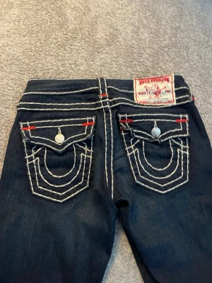True Religion mörkblå jeans  - Mörkblå jeans från True Religion med vita kontrastsömmar och detaljer i rött. Storlek 27. Buda gärna 