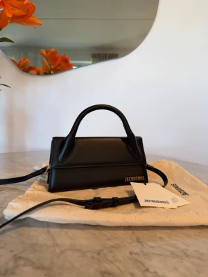 Jacquemus svart miniväska i läder - Jacquemus Le Chiquito Long i svart läder. Väskan har ett handtag upptill och en avtagbar, justerbar axelrem. Försluts med magnetlås. Guldfärgad logotyp framtill. Invändigt finns ett fack. Levereras med dustbag och taggar.  Mått: 22 cm längd, 10,5 cm höjd.  Använd fåtal gånger. Inga brister, nyskick. Köptes för 1 år sedan från MIINTO. Ny pris 9400 kr, säljes för 3950 ink frakt.  Kan även mötas upp i centrala Stockholm.