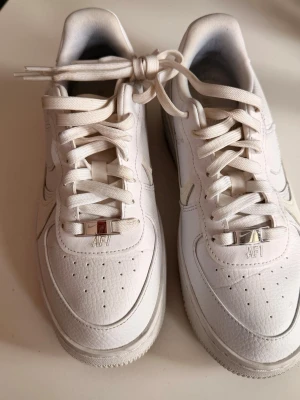 Nike Air Force 1 vita sneakers - Klassiska vita Nike Air Force 1 sneakers i lågt snitt med ovandel i läder och perforerade detaljer på tån. Skorna har vita skosnören, silverfärgade dubraes med 'AF1' och den ikoniska swoosh-loggan på sidan. Perfekta för en clean och stilren look.  Fåtal ggr använda så i nyskick .