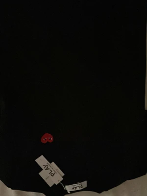 Svart t-shirt Comme des Garçons Play - Svart t-shirt från Comme des Garçons Play med det ikoniska röda hjärtat broderat på bröstet. Klassisk passform och rund halsringning. Perfekt för dig som gillar stilrena plagg med en twist.