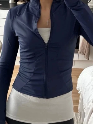 Mörkblå sportjacka med dragkedja - Slimmad mörkblå sportjacka med hel dragkedja framtill och lång ärm. Jackan har hög krage och är tillverkad i ett stretchigt, följsamt material som passar perfekt till träning eller aktiva dagar.