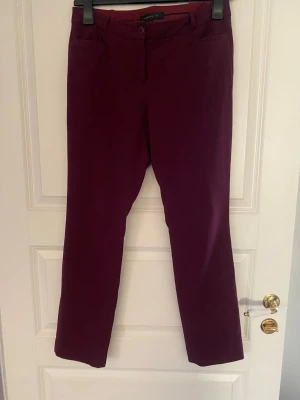 Vinröda kostymbyxor från STOCKH LM - Snygga vinröda kostymbyxor från STOCKH LM i rak modell. Byxorna har klassisk midja, hällor för skärp och stängs med knapp och dragkedja. Perfekta för en stilren look och lätta att matcha med olika toppar.