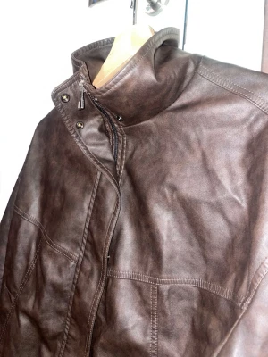 Brun skinnjacka med hög krage från BERSHKA - Snygg brun skinnjacka med hög krage och dragkedja framtill. Jackan har två sidofickor. Aldrig använd har hängt i mitt jack skap. Upptäckte en defekt på jackan en liten skråma. Bild finns på sida 5. Annars är den som ny skick🤎