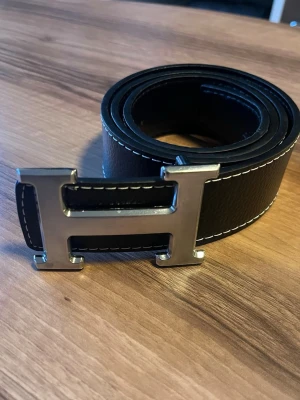 Svart h bälte med silver spänne - Längd ca120-125 cm, går att göra fler hål. Nyskick
