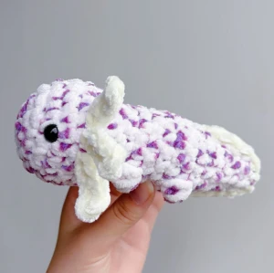 Virkad lila/vit axolotl - Lila/vit virkad axolotl – handgjord & unik💜🤍🧶 Superfin, mjuk och söt liten axolotl i lila/vit, perfekt som present eller för att ge lite extra charm till hyllan, soffan eller skrivbordet! 	•	Handgjord med kärlek 💜🤍 	•	Virkad i mjukt garn 	•	Ca 17-18cm lång 	•	Unik – bara ett exemplar!  ✨ Pris: 150 kr ✨  Passar både som prydnad och kramdjur 🧸OBS! Dessa innehåller säkerhetsögon som ej är rekommenderade för barn under 3 år!