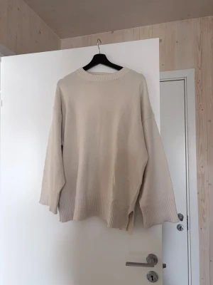 Oversized beige stickad tröja - Säljer en oversized stickad tröja i beige med breda ribbade muddar vid ärmslut och nederkant. Tröjan har rund halsringning och en avslappnad passform, perfekt för lager-på-lager. Materialet känns mjukt och bekvämt.