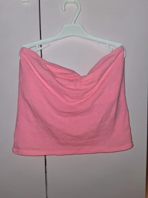 Rosa bandeau tubtopp - Säljer en söt rosa bandeau tubtopp med draperad detalj framtill. Toppen är axelbandslös och har en mjuk, bekväm passform. Perfekt att styla med jeans eller kjol för en trendig look.