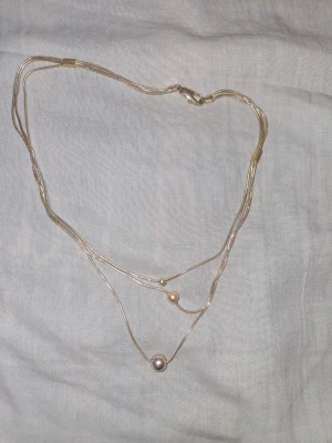 Silverfärgat halsband med pärlor - Stilrent halsband i silverfärg med tunna kedjor i flera lager och tre små pärlor i olika storlekar. Perfekt för att ge en elegant touch till din outfit. Passar dig som gillar minimalistiska smycken.