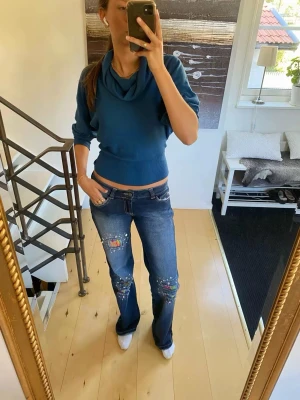 Blå bootcut jeans med färgstänk - Coola vintage jeans med låg midja och coola detaljer. Snygga bakfickor med knappar på!! Raka/bootcut Midjemått ca 39/40 cm Innerbenslängd ca 79 cm Stretchiga i midja