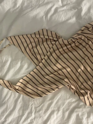 Beige topp med bruna ränder - Snygg topp i beige med tunna bruna ränder. Klassisk modell med smala axelband och låg rygg. Tillverkad i stretchigt material som sitter skönt på kroppen. 🥰