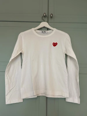 Vit långärmad tröja från Comme des Garçons - Säljer min sambos vite långärmade tröja från Comme des Garçons PLAY. Rött hjärta broderat på bröstet. Rund halsringning & tillverkad i mjuk bomull. Köpt på Farfetch & kvitto finns.