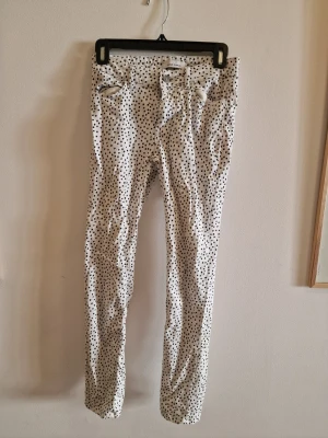 Prickiga jeans från Samsøe Samsøe - Snygga vita jeans med svarta prickar från Samsøe Samsøe. Modellen är slim fit med klassisk femficksdesign och bälteshällor. Jeansen har knapp och dragkedja framtill och är tillverkade i ett mjukt bomullstyg. Perfekta för dig som vill sticka ut med din stil.