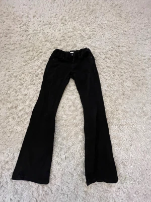 Svarta bootcut jeans - Svarta jeans med bootcut passform och klassiska fem fickor. Jeansen har bälteshällor och knappstängning framtill. Perfekta för dig som gillar en tidlös och avslappnad stil.