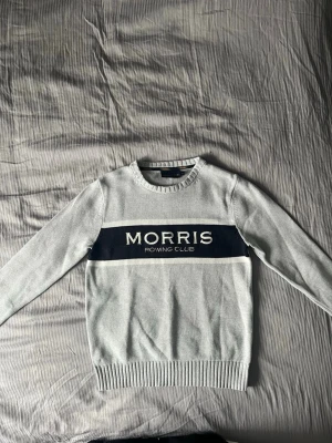 Ljusgrå Morris Rowing Club tröja - Är M men sitter som S. Snygg ljusgrå tröja från Morris med mörkblå panel och vit text 'Morris Rowing Club' över bröstet. Tröjan har rund halsringning, långa ärmar och ribbade muddar. Perfekt för en sportig och stilren look. 