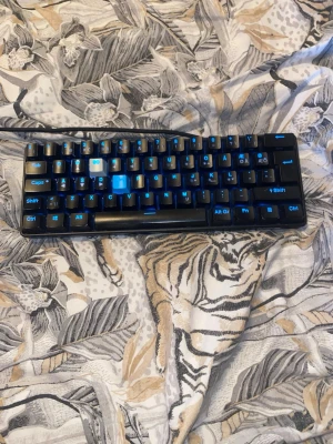 NOS C250 mekaniskt tangentbord - Säljer ett NOS C250 mekaniskt tangentbord med blå LED-belysning. Tangentbordet är kompakt och svart med tydliga blå symboler på tangenterna. Perfekt för gaming eller arbete vid datorn. Tillverkat i plast och ansluts med kabel.