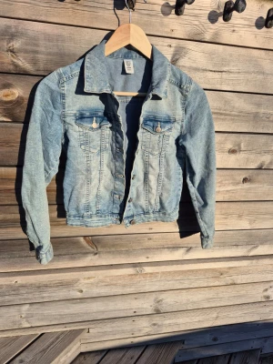 Ljusblå croppad jeansjacka - Ljusblå jeansjack. Jackan har två bröstfickor med lock och silverfärgade knappar framtill. Finns två små fläckar som jag inte har försökt atr få bort. 