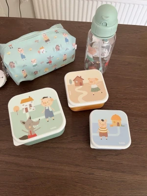 Set med barnlådor och vattenflaska - Säljer ett gulligt set från Tutete med tre matlådor i olika storlekar, en vattenflaska och en necessär. Alla delar har motiv från sagan om de tre små grisarna i pastellfärger. Perfekt för utflykter eller förskolan. Materialet är plast och textil.
