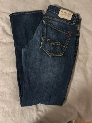 Mörkblå Replay jeans med kontrastsömmar - Snygga mörkblå jeans från Replay med klassisk femficksmodell och kontrastsömmar. Jeansen har en liten sliten detalj framtill och Replay-märke på bakfickan. Materialet är denim i bomull med en skön passform och lätt tvättad look.