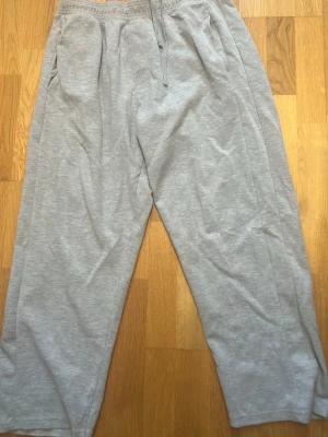 Grå mjukisbyxor från pullbear - Ett par klassiska grå mjukisbyxor med resår i midjan och dragsko. Byxorna har två sidofickor fram och en bakficka. De är raka i modellen och tillverkade i mjukt bomullsmaterial, perfekta för en avslappnad stil.