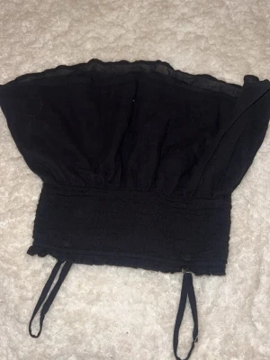 Svart smockad linnetopp Gina Tricot - Svart linnetopp från Gina Tricot med smockad midja och tunna axelband. Toppen har en luftig och lätt form, perfekt för varma dagar. Enkel och stilren design som är lätt att matcha med olika outfits.