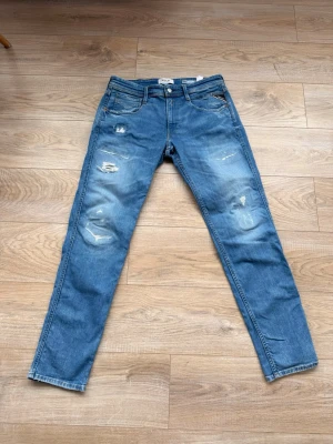 Blå slitna jeans från Replay - Säljer ett par blå jeans från Replay med slitningar på framsidan. Dem är i mycket bra skick och bär storleken 31/32. Jag själv är 184 och dem sitter bra på mig så du bör vara 178-186