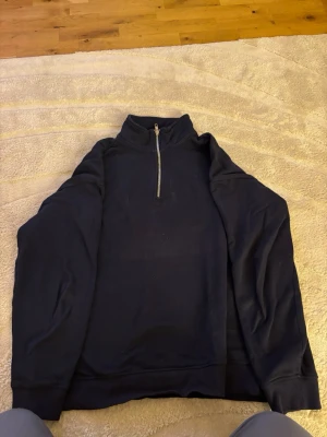 Mörkblå halvzip tröja - Mörkblå långärmad tröja med halv dragkedja i halsen. Tröjan har en enkel och stilren design med ribbade muddar vid ärmslut och nederkant. Perfekt för lager-på-lager och chill vardagsstil.