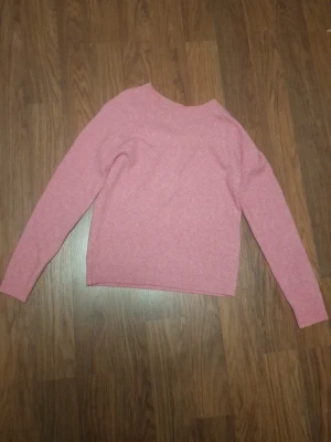 Rosa stickad tröja med rund hals - Mysig rosa stickad tröja med rund hals och långa ärmar. Tröjan har en enkel och klassisk design med ribbstickade muddar vid ärmslut och nederkant. Perfekt för att hålla värmen under kyliga dagar.