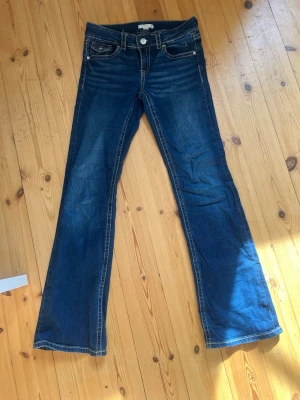 Mörkblå bootcut jeans med fickdetaljer från Gina Tricot - Snygga mörkblå bootcut jeans från Gina Tricot, i strl 164 med kontrastsömmar och coola bakfickor med lock och knapp. Klassisk femficksmodell och låg midja. Perfekta för en avslappnad och trendig look.