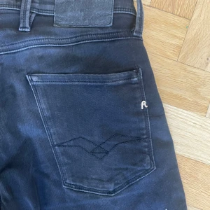 Svarta Replay jeans slim fit - Säljer ett par svarta Replay jeans med snyggt broderade bakfickor och diskret Replay-logga. Jeansen har smal passform och är i Storleken 30/32