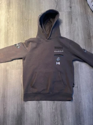  Hoodrich hoodie - Säljer en grå hoodie från Hoodrich med broderade och tryckta detaljer på bröstet, ärmarna och huvan. Hoodien har en stor magficka och klassisk huva med Hoodrich-logga. Tillverkad i mjukt bomullsmaterial, perfekt för en avslappnad streetwear-look.