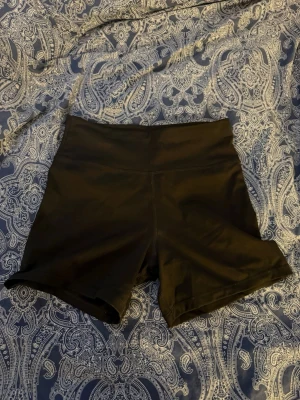 Svarta höga träningsshorts från Stadium - Säljer ett par svarta, högmidjade träningsshorts från Stadium. De har en bred linning och är tillverkade i stretchigt material som passar perfekt för gymmet eller löprundan. Snygg och enkel design utan synliga detaljer förutom loggan bak.