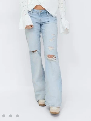 Ljusblå slitna bootcut jeans - Säljer ett par ljusblå bootcut jeans med slitningar och hål på låren och knäna. Jeansen har klassisk femficksmodell och låg midja. Perfekta för en avslappnad och trendig look. Helt nya, aldrig använda. Prislappen kvar 🥰