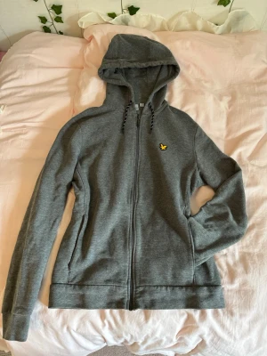 Mysig snygg grå hoodie från Lyle & Scott - Säljer en grå hoodie från Lyle & Scott med dragkedja framtill och klassisk gul logga på bröstet. Hoodien har snörning i huvan och två fickor på sidorna! Tillverkad i mjukt bomullsmaterial och har ribbade muddar vid ärmar och nederkant❣️Riktigt snygg och passar perfekt till alla plagg. Bara att kasta på🙌🏻Storlek S. Inga defekter! Orginalpris runt 899kr💞
