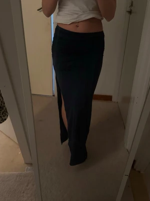 Mörkblå  långkjol med slits - Säljer en mörkblå långkjol med hög slits på ena sidan. Kjolen har en tight passform och är perfekt för dig som vill ha en stilren och enkel look. Materialet känns mjukt och följsamt mot kroppen.