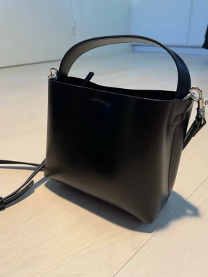 Handväska NA-KD - Minimalistisk och stilren svart handväska från NA-KD. Klassisk design med både kort handtag och avtagbar, justerbar axelrem. Väskan har ett rymligt huvudfack samt en praktisk innerficka med dragkedja i mitten för extra förvaring. Knappt använt! Därför säljer jag den❤️