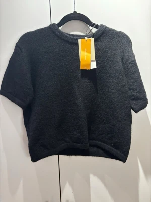 Svart stickad croppad topp H&M - Svart stickad croppad topp från Gina Tricot med korta ärmar och rund hals. Toppen har en mjuk och lite luddig yta som ger en mysig känsla. 