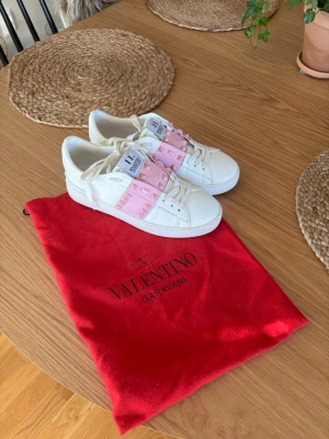 Valentino Rockstud sneakers rosa/vit - Snygga vita Valentino Garavani Rockstud sneakers som är köpta av en tjej här på Plick så vet inte ifall de är äkta eller inte. Dom har en liten difekt som syns på sista bilden men är inget som syns när man har på sig dem. Man får med dustbag och extra snöre.