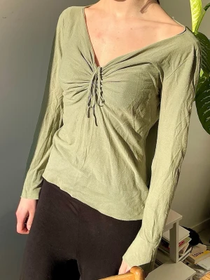  EMPORIO ARMANI Y2K top - olivgrön med snörning - EMPORIO ARMANI, från 2000s-era. En lace up top, olivgrön  med lång ärm och djup v-ringning. Toppen har snygg snörningsdetalj framtill som man kan knyta upp. Fint skick. Kan stylas off shoulder. 100% bomull. Storlek 46