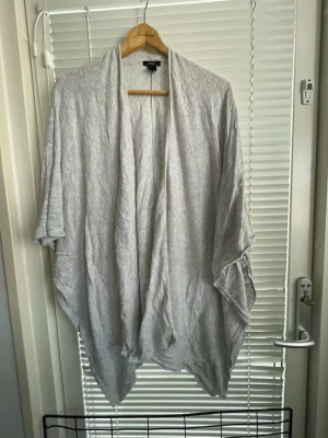 Ljusgrå öppen kofta från Lindex - Ljusgrå, tunn och öppen kofta från Lindex i storlek XS/S. Koftan har ett avslappnat, flödande snitt med kortare ärmar och faller snyggt längs kroppen. Perfekt att slänga över en topp för en chill look.