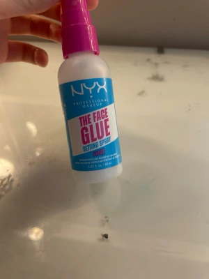 NYX The Face Glue Setting Spray - NYX The Face Glue Setting Spray är en ansiktsspray som fixerar din makeup. Flaskan är vit med blå och rosa etikett och har en rosa spraypump. Innehåller 60 ml och är perfekt för att hålla sminket på plats hela dagen.