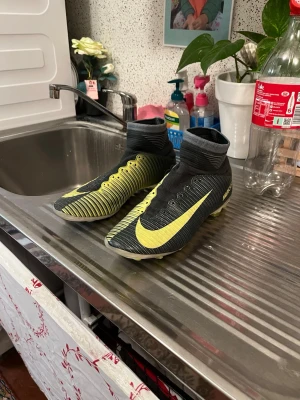 Nike Mercurial fotbollsskor svart/gul. CR7 - Säljer ett par Nike Mercurial fotbollsskor i svart och gul med hög ankelkrage och snörning. Skorna har en modern design med tydliga gula detaljer och Nike-logga på sidan. Perfekta för dig som vill ha stilrena och snabba skor på planen. Äkta CR7 Nike skor, köpte den för ungefär 1,7k. Den högre av skonen så är dobbarna lite slitna, de för art jag har använt dom jätte mycket och att har gått runt med dom på market. Snören finns med dom 