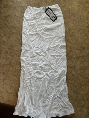 Vit långkjol - Säljer en enkel och stilren vit långkjol från new yorker. Kjolen är rak i modellen och har en mjuk resår i midjan. Tillverkad i lätt och bekväm bomull, perfekt för varma dagar. Passar till många olika stilar och är superenkel att matcha.