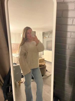 Beige kabelstickad tröja - Mysig beige kabelstickad tröja med breda ärmar och avslappnad passform. Tröjan har rund halsringning och ett klassiskt stickat mönster som ger en trendig och chill vibe. Perfekt att matcha med jeans för en enkel och snygg look.