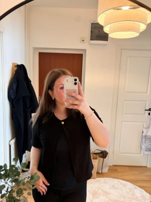 Svart kortärmad topp - Stilren svart kortärmad öppen topp med en guldknapp framtill. Ny med prislapp