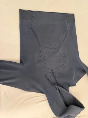 Mörkblå hoodie från Hugo Boss - Snygg mörkblå hoodie från Hugo Boss med stor, upphöjd logga på bröstet. Klassisk huva med dragsko och ribbade muddar vid ärmslut och nederkant. Tillverkad i mjukt bomullsmaterial som känns riktigt skönt mot huden. Perfekt för en avslappnad och trendig look.