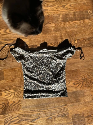 Leopardmönstrad offshoulder topp FB Sister - Säljer en snygg offshoulder topp från FB Sister med leopardmönster i svart och beige. Toppen är tight och har korta ärmar samt tunna axelband som kan knytas. Perfekt för dig som vill sticka ut lite extra!