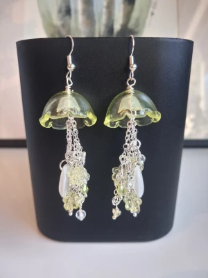 Unika örhängen maneter jellyfish  - Säljer ett par handgjorda örhängen formade som maneter i transparent ljusgul glas med silverfärgade kedjor och detaljer. Hängena har små pärlor och droppformade dekorationer som ger ett lekfullt och kreativt intryck. Perfekta för dig som gillar statement-smycken! Längd ca 6.5cm långa. Öronkroken är nickelsäker och aldrig använda 