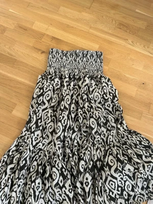 Svartvit mönstrad klänning - Svartvit klänning med grafiskt mönster och smock upptill. Klänningen har en luftig passform och är ärmlös, perfekt för varma dagar. Tillverkad i ett mjukt och lätt tyg som ger en skön känsla.