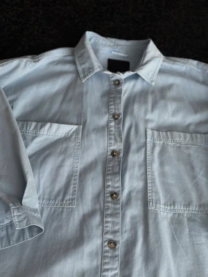 Ljusblå skjorta från 157 L - Ljusblå skjorta från 157 i mjuk bomull. Klassisk modell med två stora bröstfickor, knappar framtill och lång ärm. Perfekt oversized look och enkel att styla till olika outfits. Väldigt lös
